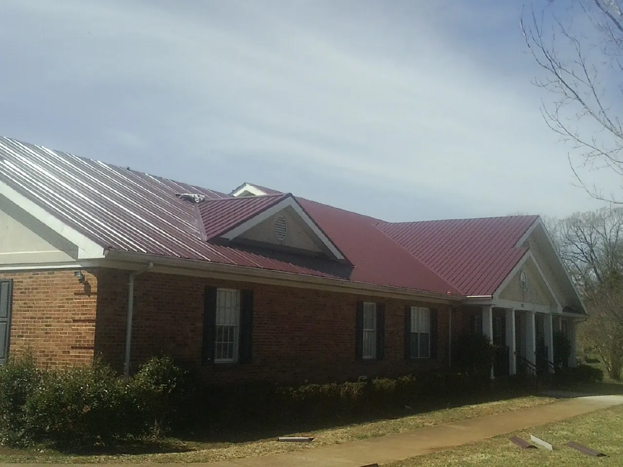 Red metal roof with gabled entries on a long brick building, from a Hail Damage Roof Repair job in Dunellen