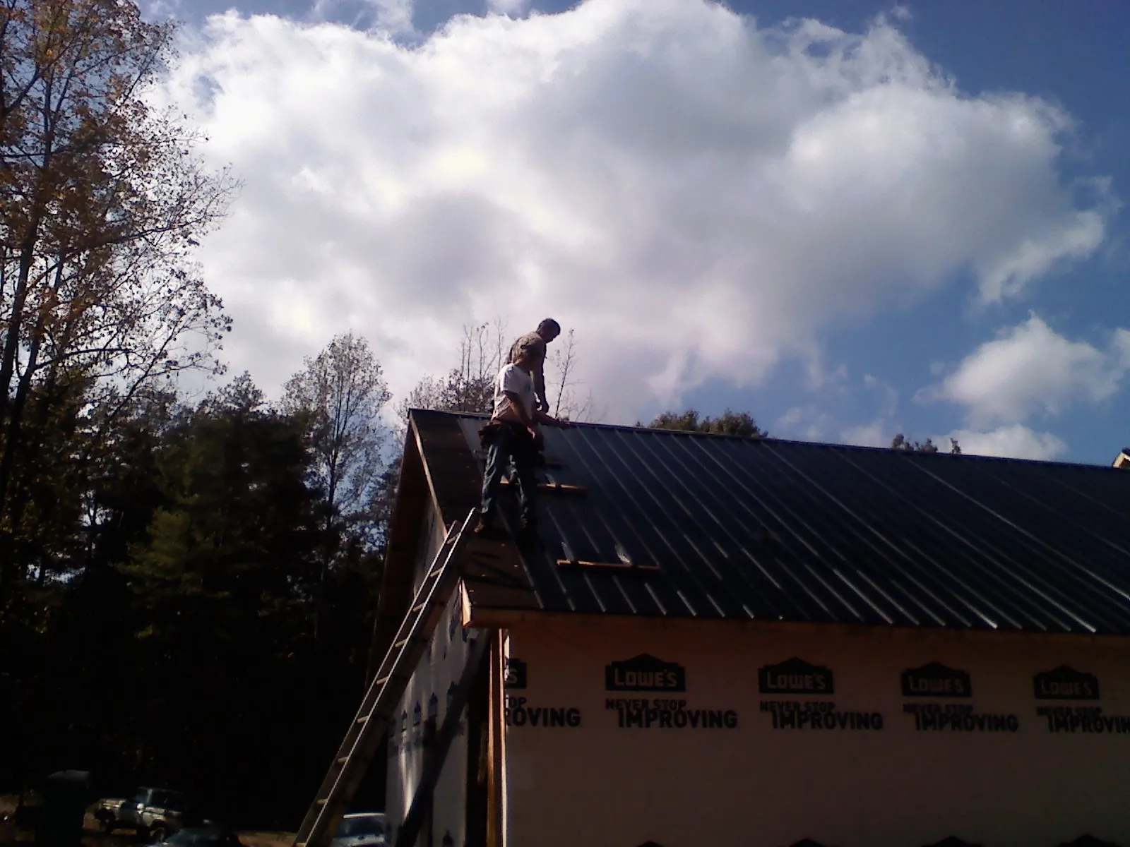 Roofer fastening dark metal panels high against a cloudy sky, from a Roof Inspection job in Dunellen