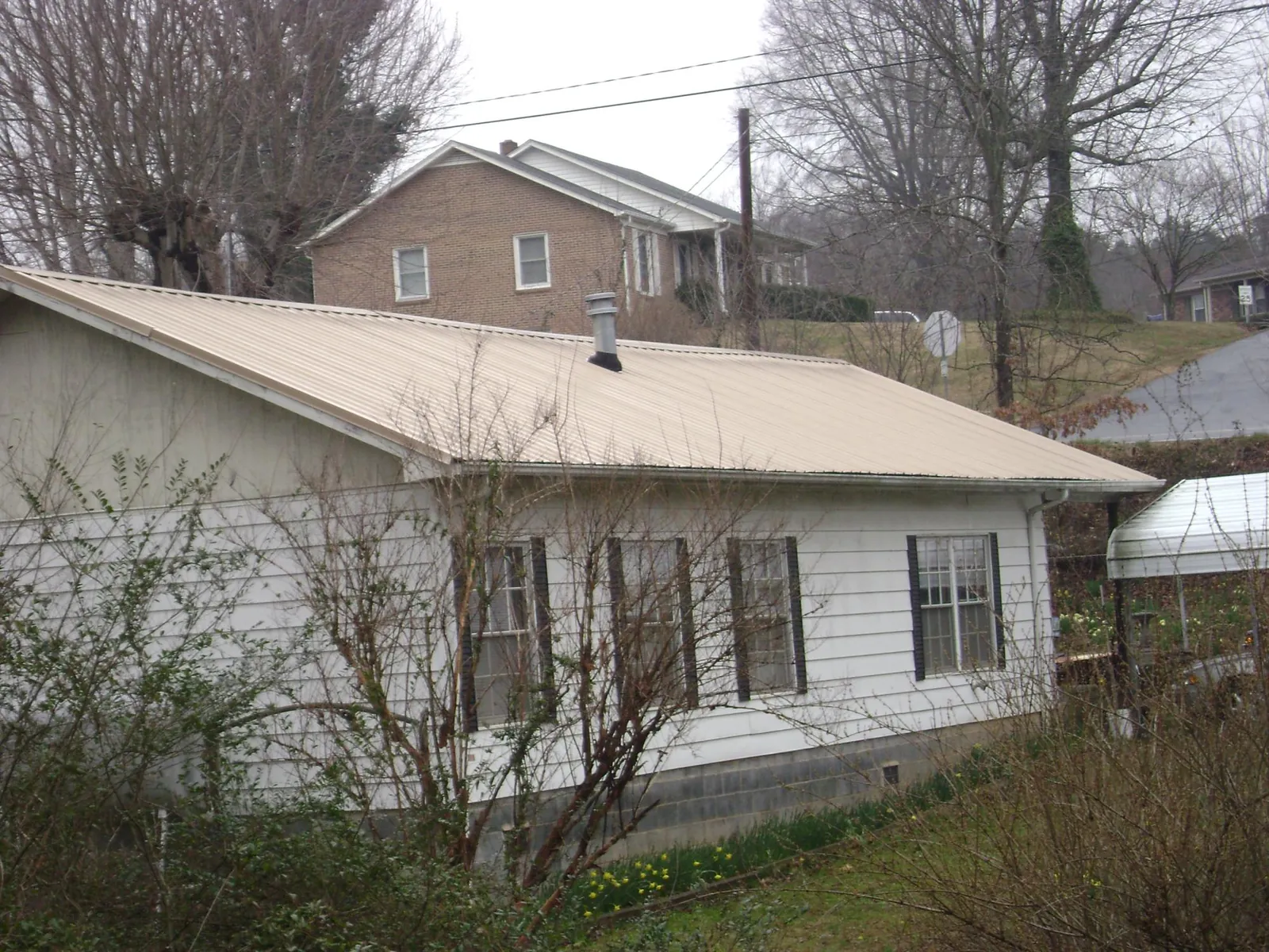 Tan metal roof on a white sided house set into a hillside — Commercial Roofing by Roofing Brothers in Dunellen